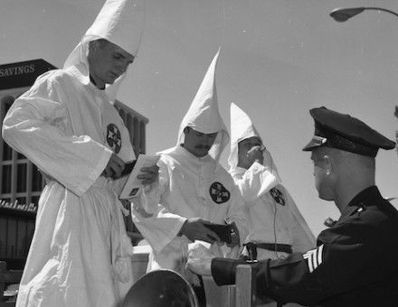 A police officer checks the ID of three members of the Ku Klux Klan in Panorama City, California, 18 September 1966. University of California, Los Angeles. Library. Department of Special Collections (CC BY 4.0).